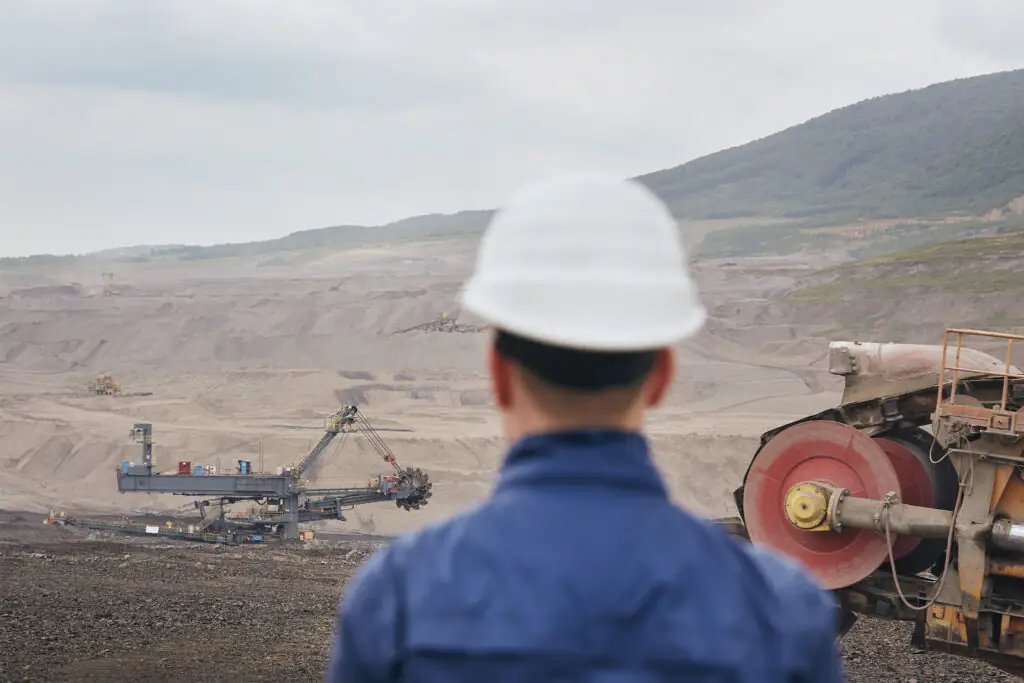 Coal mining in surface mine. Miner looking on the huge excavator.